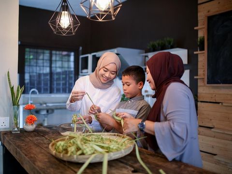 Mother and sister with brother making food in kitchen during eid celebration in Malaysia