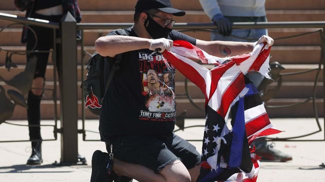 A participant destroys a thin blue line American flag used to honor police officers during a protest outside the State Capitol over the death of George Floyd, a handcuffed black man in police custody in Minneapolis, Friday, May 29, 2020, in Denver. More than 1,000 protesters walked from the Capitol down the 16th Street pedestrian mall during the protest. (AP Photo/David Zalubowski)