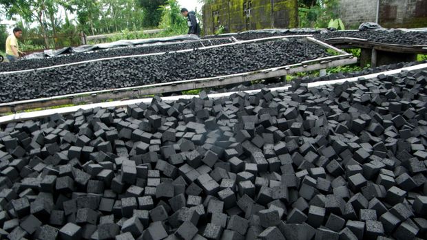 Pekerja menutup briket yang sedang dalam proses penjemuran menggunakan plastik di industri briket rumahan 
