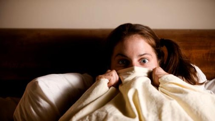 Frightened Woman in Bed with the Sheets Pulled Up to her Face