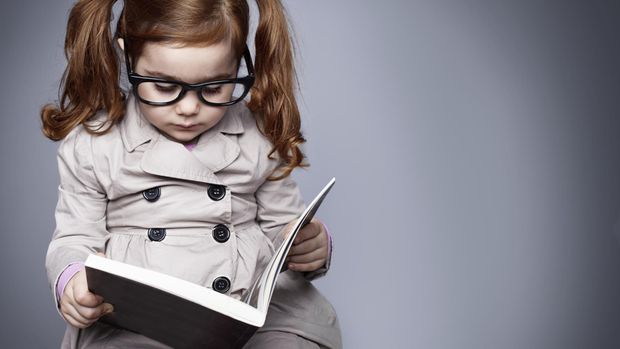 Anak perempuan berkacamata sedang membaca buku.