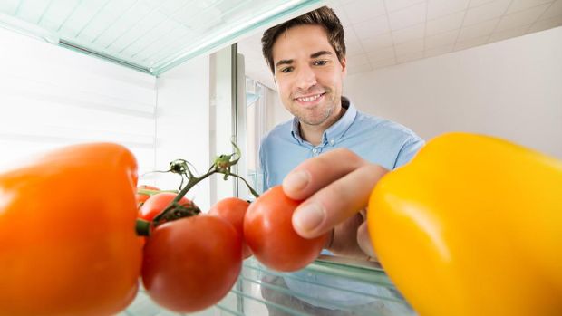 Handsome Man Looking At Tomatoes And Bell Pepper View From Inside The Refrigerator At Home