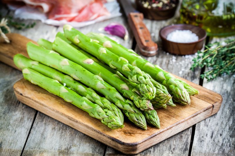 Fresh organic asparagus on a cutting board with Parma ham on a rustic table