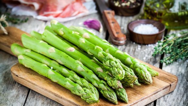 Fresh organic asparagus on a cutting board with Parma ham on a rustic table