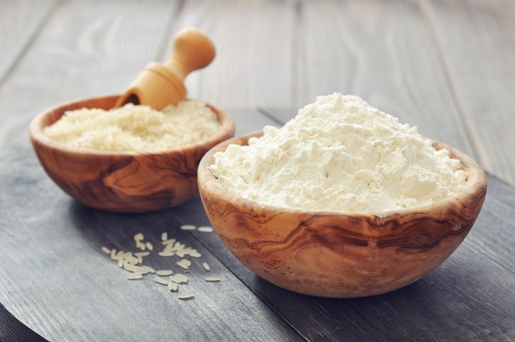 Raw rice and flour in bowls with scoop on wooden background