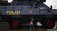 Seorang suporter berteduh di samping kendaraan taktis Polri.