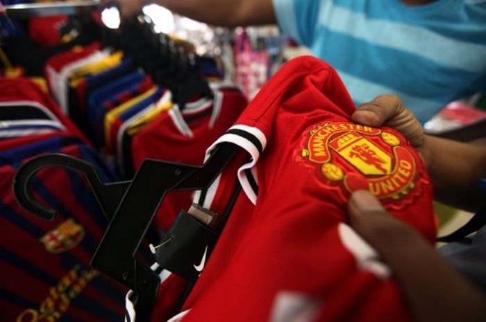 A Malaysian customers checks the logo of English football club Manchester United on a jersey before a purchase at a roadside shop in Kuala Lumpur on August 17, 2011. Legendary English football club Manchester United plans to tap its massive Asian fan base and raise up to $1 billion by listing 30 percent of its shares in Singapore AFP PHOTO / Mohd Rasfan / AFP PHOTO / MOHD RASFAN