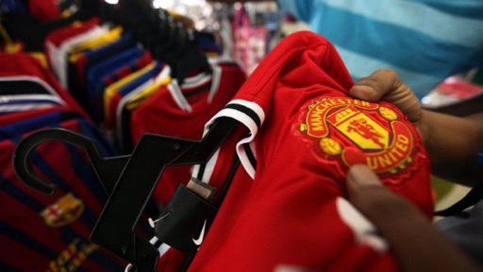 A Malaysian customers checks the logo of English football club Manchester United on a jersey before a purchase at a roadside shop in Kuala Lumpur on August 17, 2011. Legendary English football club Manchester United plans to tap its massive Asian fan base and raise up to $1 billion by listing 30 percent of its shares in Singapore AFP PHOTO / Mohd Rasfan / AFP PHOTO / MOHD RASFAN