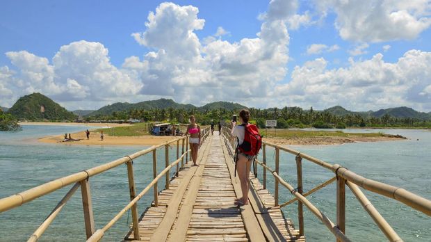 Dua orang wisatawan asing melewati jembatan bambu menuju pantai Seger kawasan KEK Mandalika di Desa Kuta, Kecamatan Pujut, Praya, Lombok Tengah, Nusa Tenggara Barat, Minggu (30/4). ANTARA FOTO/Ahmad Subaidi/17.