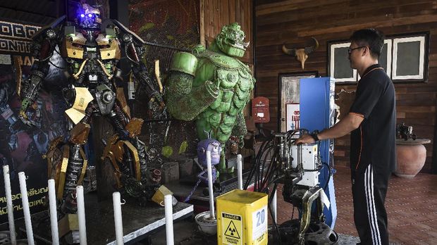 This photo taken on June 13, 2017 shows artist Phairote Thanomwong operating a mechanical Transformer at Ban Hun Lek, a metalworks shop renowned for giant statues of Transformers, the Hulk and other pop icons, in the central Thai province of Angthong.As Buddhist temples across Thailand struggle to stay relevant in the modern age, some monks are drawing on a tried-and-true magnet for children: superheroes. / AFP PHOTO / LILLIAN SUWANRUMPHA