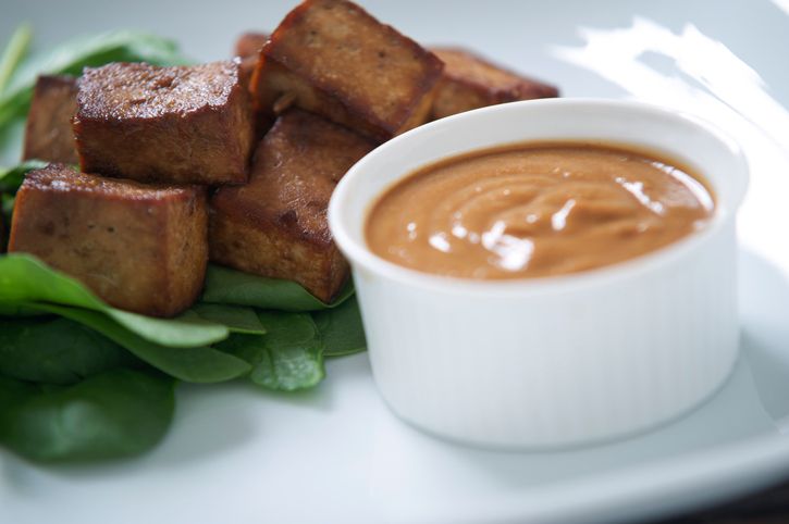 Indonesian marinaded tofu with peanut satay sauce on a small bed of spinach.