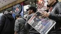 Saking panjangnya antrean, salah satu fans PSG sampai ada yang membawa koran sembari menunggu kesempatan masuk toko. (Foto: Philippe Lopez/AFP)
