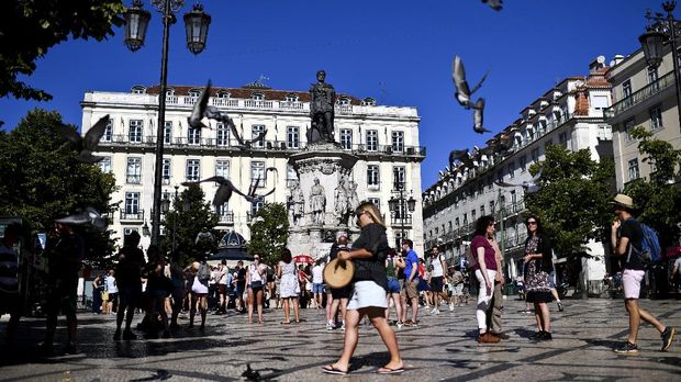 Pigeons fly over tourists gathering at Camoes square, Lisbon, on August 2, 2017. / AFP PHOTO / PATRICIA DE MELO MOREIRA