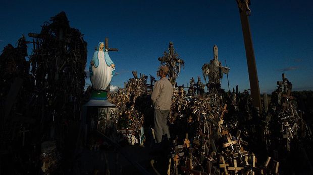 A local man prays in front of the statue of the Virgin Mary surounded by crosses on the 