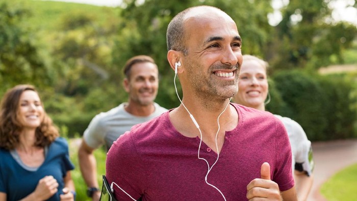 Portrait of a happy cheerful man listening to music while jogging. Man listening to music while jogging with group. Happy trainer in park running with team.r