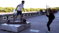 Seorang pria terlihat berpose di atas bagian yang tersisa dari patung Messi yang dirusak. Meski tinggal menyisakan telapak kaki, patung Messi masih jadi objek foto. Foto: Marcos Brindicci/Reuters