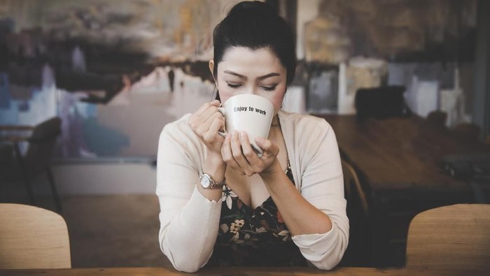 young chinese woman sitting next to windows in cafe. minum kopi