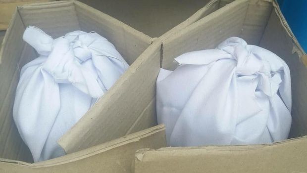 Tumbal di dalam kardus yang berisi kain moro, tanaman, dan buah-buahan