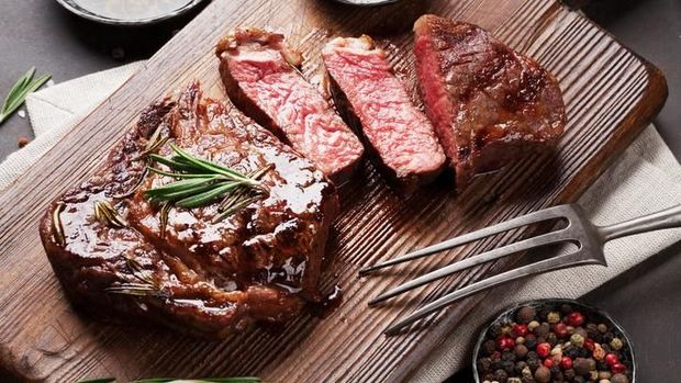 Sliced medium rare grilled Steak Ribeye with french fries on serving board block on wooden background