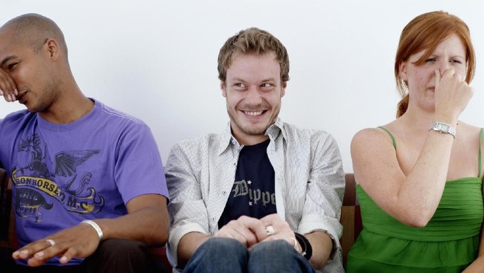 Young man, smiling, sitting between man and woman holding noses