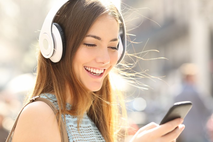 Portrait of a happy girl listening music on line with wireless headphones from a ponsel cerdas in the street in a summer sunny day