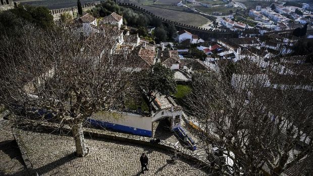 A man stands at the entrance of the 'Pousada do Castelo' inn located in the medieval town of Obidos, central Portugal, on February 9, 2018.To attract visitors to places not currently on their radar, and help ensure a constant year-round flow of tourists, Portugal's socialist government is leasing abandoned monasteries, forts and other historic sites to private groups to be turned into hotels and other leisure centres. / AFP PHOTO / PATRICIA DE MELO MOREIRA