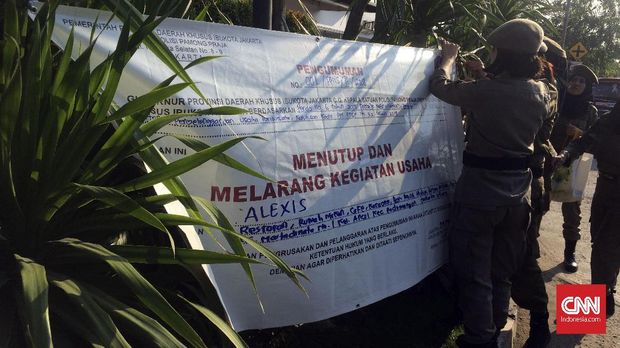 Petugas Satpol PP memasang spanduk pengumuman penutupan Hotel Alexis, Kamis (29/3).