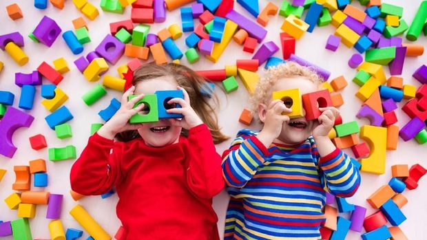 Happy preschool age children play with colorful plastic toy blocks. Creative kindergarten kids build a block tower. Educational toys for toddler or baby. Top view from above.