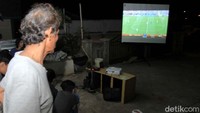 Pemudik menyaksikan laga piala dunia yang ditampilkan di layar proyektor berwarna putih di halaman rumah warga.