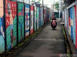 Pengendara motor melintas diantara gang berhiaskan mural-mural Piala Dunia.