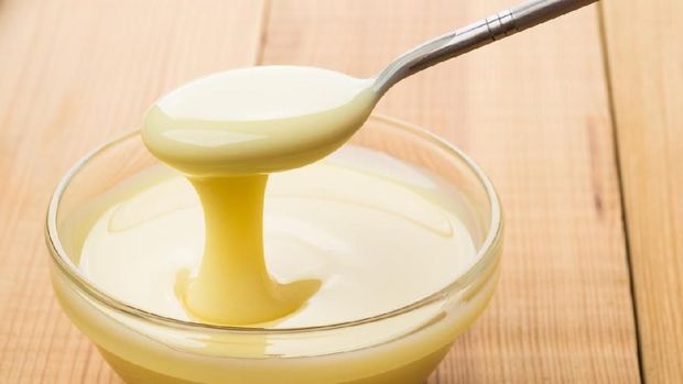 Ilustrasi Susu kental manis Transparent bowl with condensed milk and teaspoon on wooden table