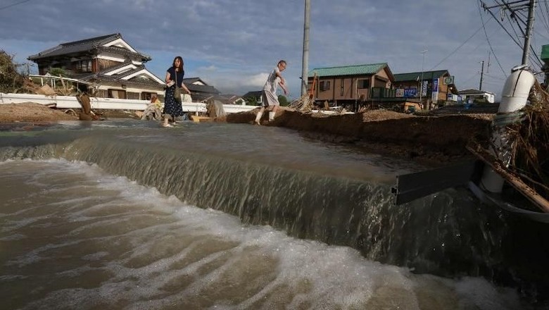 Korban Tewas Akibat Banjir di Jepang Nyaris 100 Orang, 58 Hilang Warga Jepang melewati jalanan yang masih digenangi banjir (AFP PHOTO/JIJI PRESS - via detik.com)