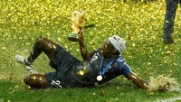 Benjamin Mendy berselancar di atas rumput sambil memegang erat trofi. REUTERS/Kai Pfaffenbach.