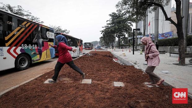 Warga menginjak bebatuan yang ditempatkan di area tanah yang hendak ditanami rerumputan di trotoar.