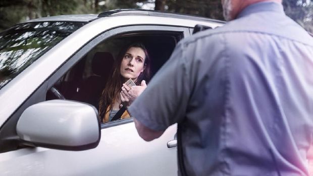An on duty law enforcement officer, working hard at providing justice, keeping the peace, and making the country a safer place.  Here he inspects the drivers license of a person he has pulled over for speeding, given them a stern warning about the risk and danger of their behavior and the cost of a potential ticket.