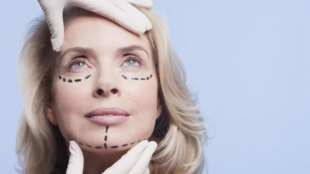 Rubber-gloved hands holding woman's face with dotted lines