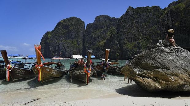 Teluk Maya di Pulau Koh Phi Phi This photo taken on April 9, 2018 shows a tourist sitting on a rock at the edge of Maya Bay on the southern Thai island of Koh Phi Phi. Across the region, Southeast Asia's once-pristine beaches are reeling from decades of unchecked tourism as governments scramble to confront trash-filled waters and environmental degradation without puncturing a key economic driver. / AFP PHOTO / Lillian SUWANRUMPHA