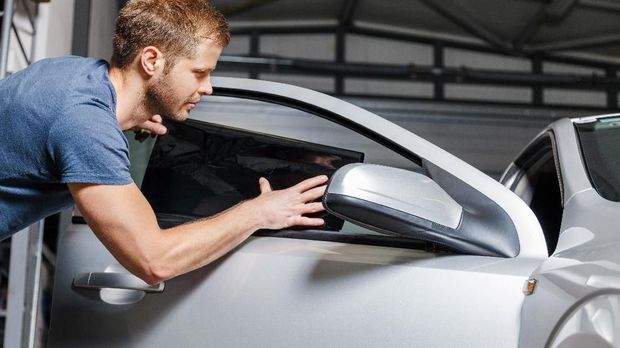 Applying tinting foil onto a car window in a workshop