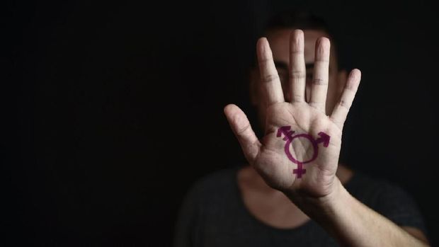 closeup of a transgender symbol painted in the palm of the hand of a young caucasian person against a black background, with a negative space on the left