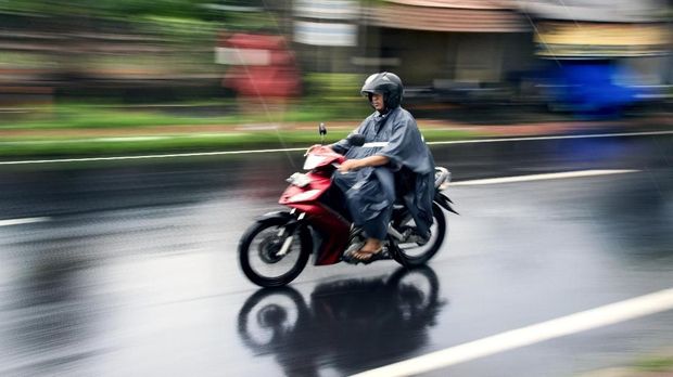 Bali, Indonesia - June 7, 2017: Balinese male riding a motorcycle under the rain at Ubud Bali Indonesia