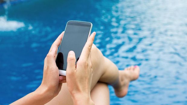 Girl using phone by the swimming pool, first person