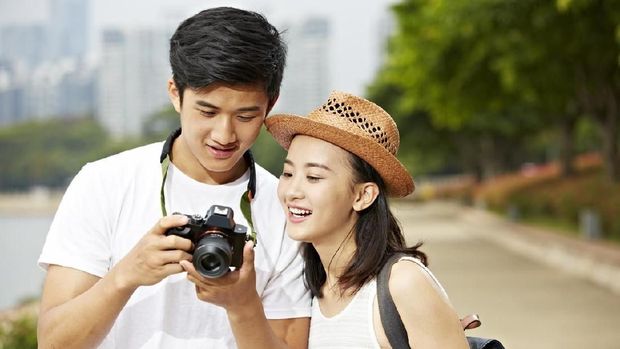 young asian couple tourists looking at camera's monitor checking pictures taken