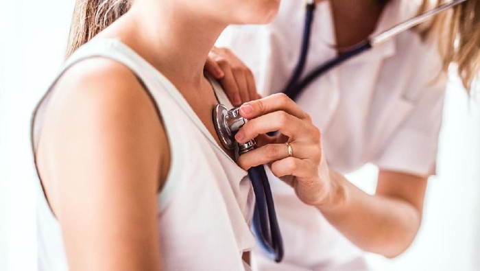 Ilustrasi dokter-pasien An Asian girl is indoors in a hospital room. She is wearing casual clothing. An Asian female doctor wearing medical clothing is checking her heartbeat with a stethoscope.