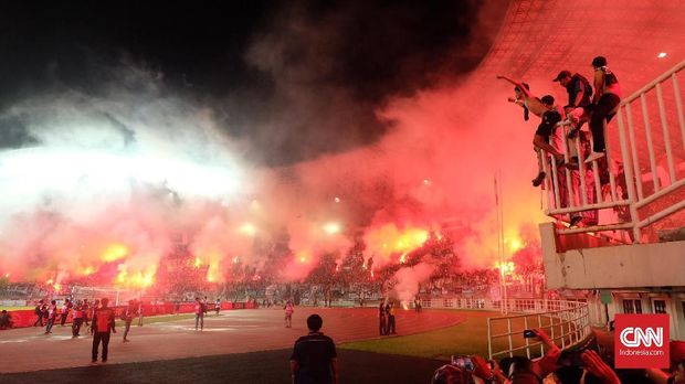 Tribune penonton memerah akibat pembakaran suar oleh suporter.