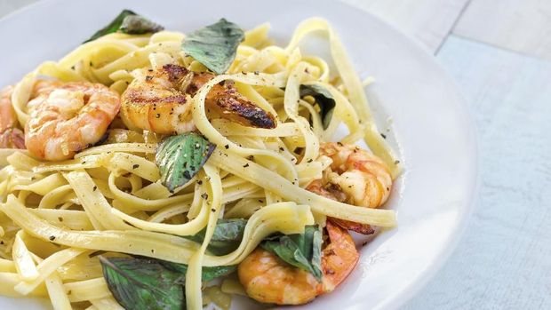 Pasta with prawns and basil leaves on white plate.