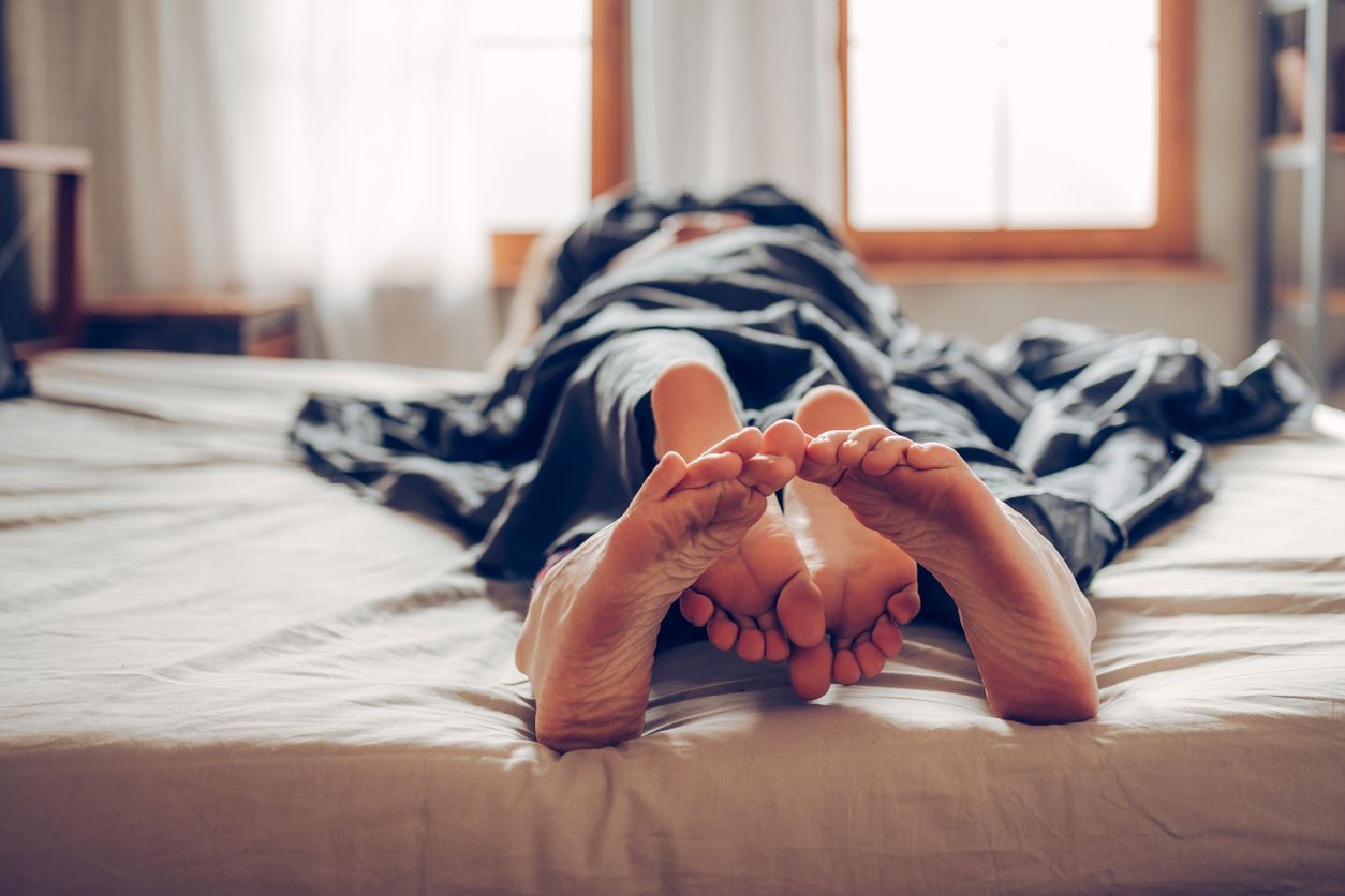 Closeup side view of late 20's couple kissing in bed which probably leads to some love making. They are both still wearing pajamas and everything is decent.