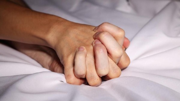 Couple in bed holding hands passionately