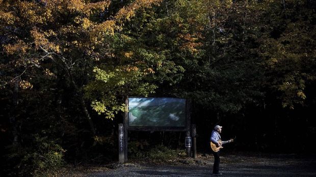 In this picture taken on November 1, 2018 Japanese musician Kyochi Watanabe plays his guitar as he poses for a photo at the entrance of Aokigahara Forest, known as Suicide Forest, in Narusawa village, Yamanashi prefecture. - Japanese musician Kyochi Watanabe has waged an eight-year battle to try to turn back people who come to what is known as Japan's 
