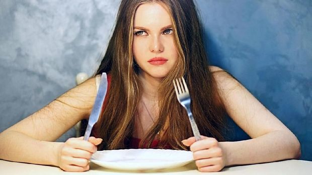 A hungry caucasian girl is waiting with a plate.  Food safety picture.