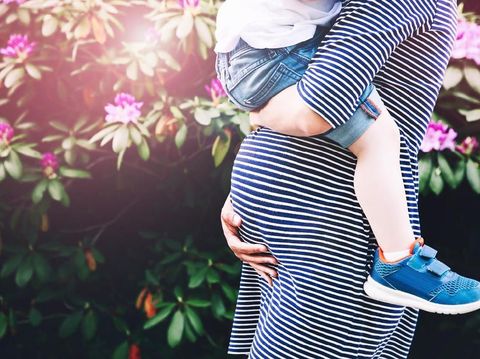 Pregnant woman with child. Mother and son on nature background, close-up. Child boy is sitting on belly of his mother, who pregnant for second time. Pregnancy, new life, family, parenthood concept.